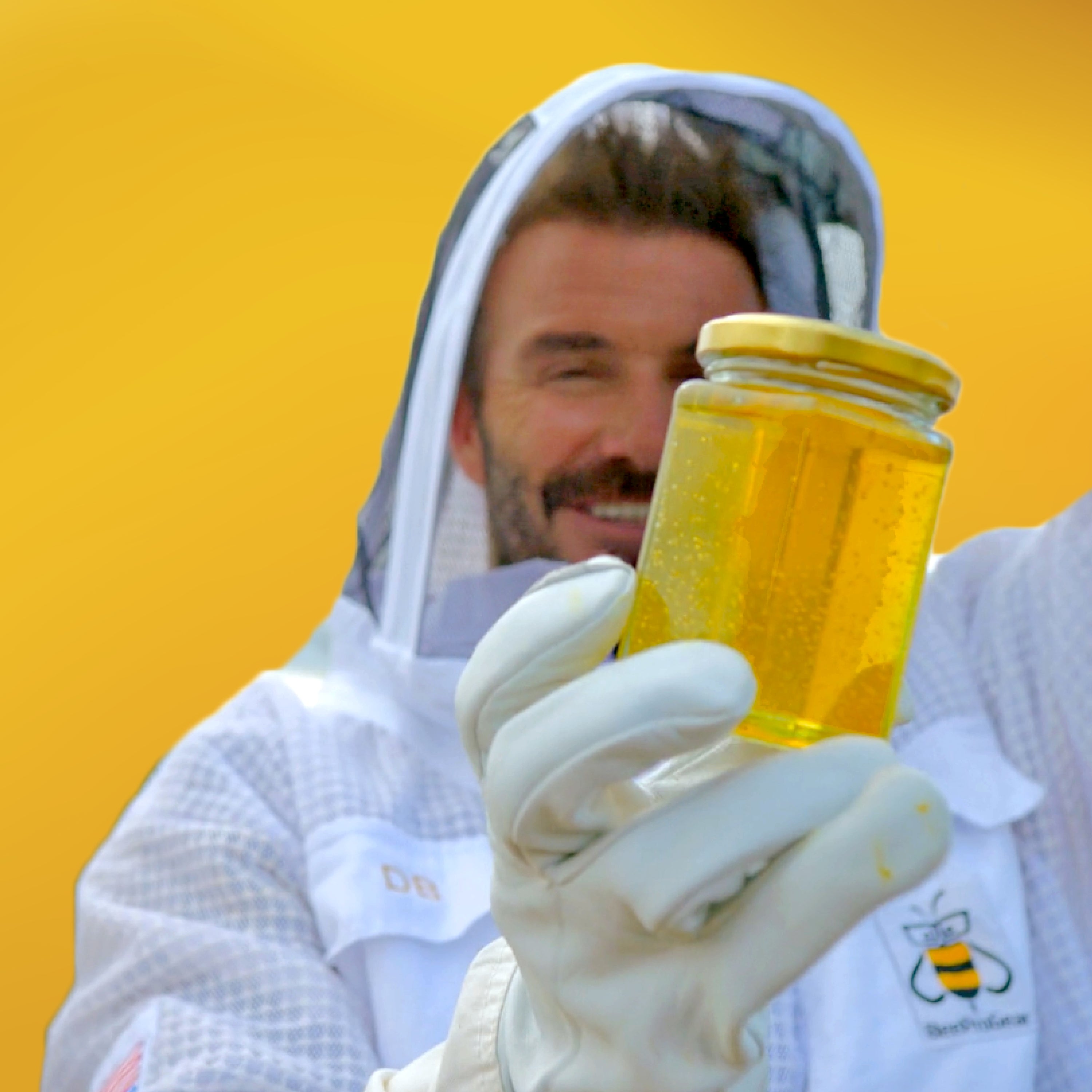 David Beckham in a beekeeping suit, smiling, while holding up a jar of honey against a yellow background